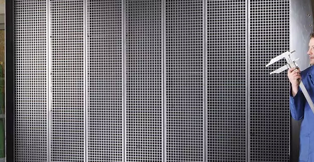 Ouvrier qualifié en équipement de sécurité installant une protection modulaire sur radiateur industriel haute température à l'aide d'une visseuse sans fil dans un atelier de production